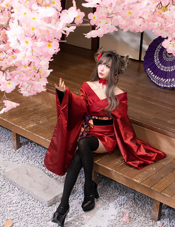 縁台に腰掛け、庭の桜を見上げる赤い着物の女性の写真。