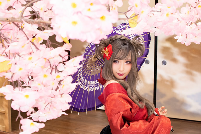 桜の木の下で和傘を指して振り返る赤い着物の女性の写真。